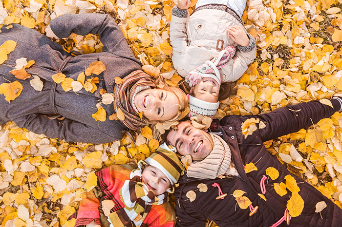 family of four laying on yellow autumn leaves smiling