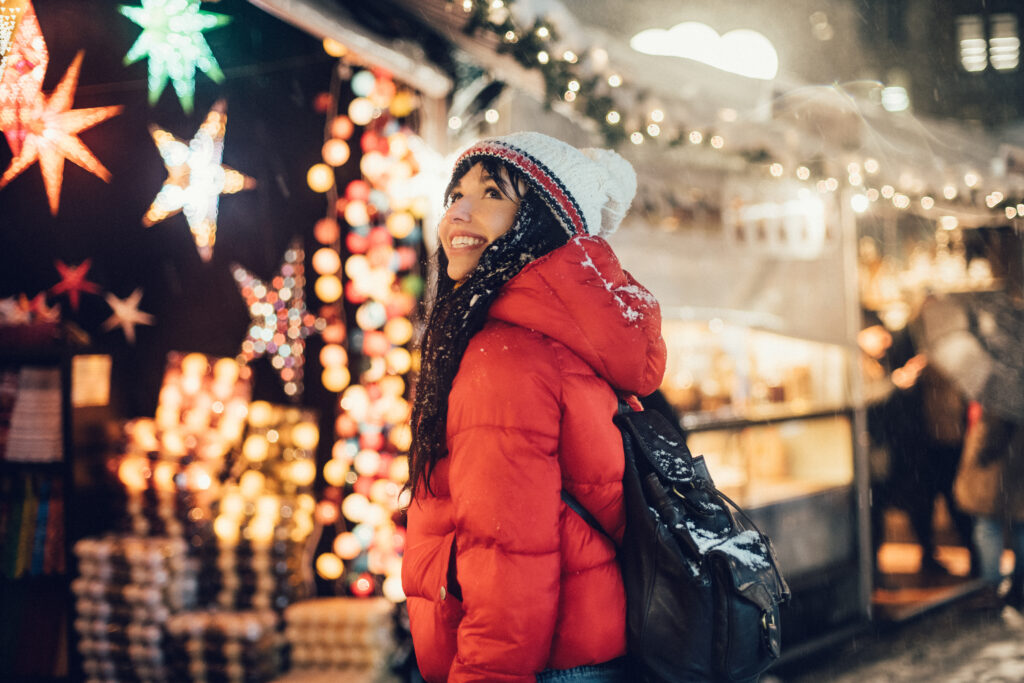 Beautiful happy woman looking for a present on Christmas city fair during snow storm
