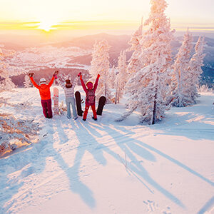 Group of snowboarders on snowy mountain with trees and sunset in background